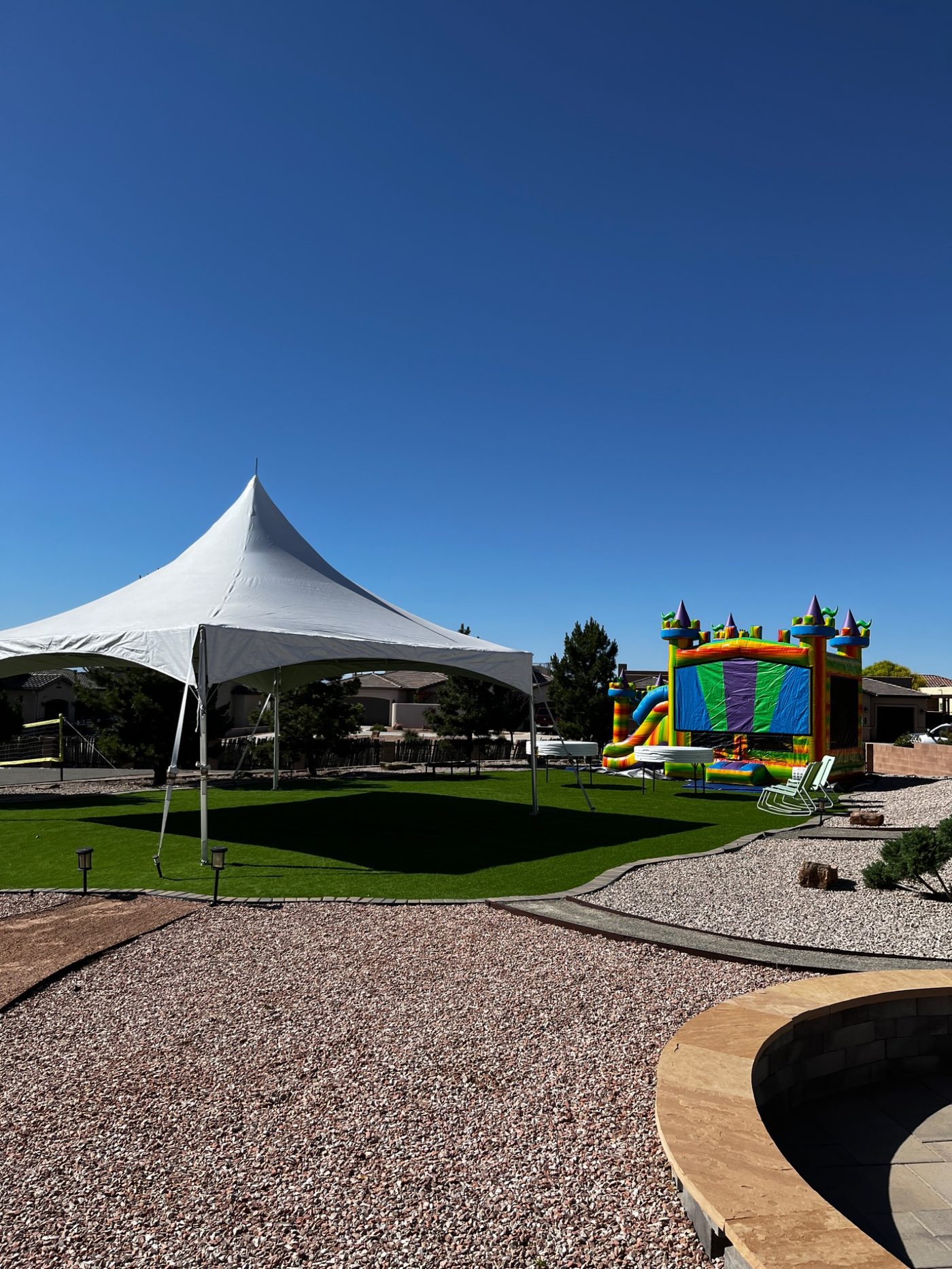 High peak tent and colorful bounce house set up for a backyard party